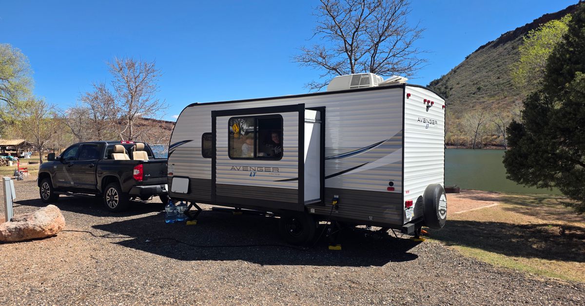 A scenic daytime camping setup with a caravan and truck by a lake in a natural setting.