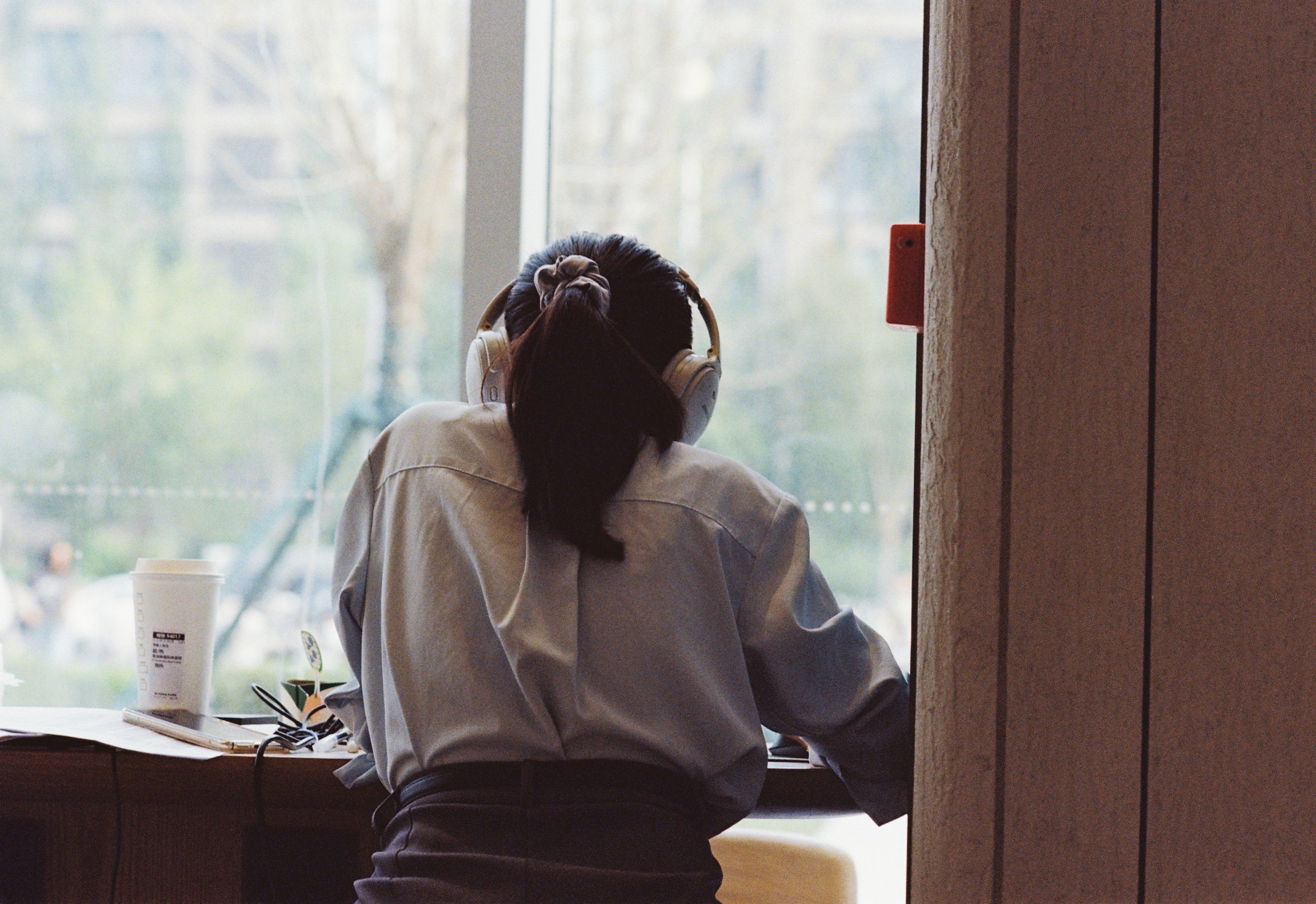 A woman wearing headphones studies by a window in a Beijing cafe, capturing a tranquil and focused moment.