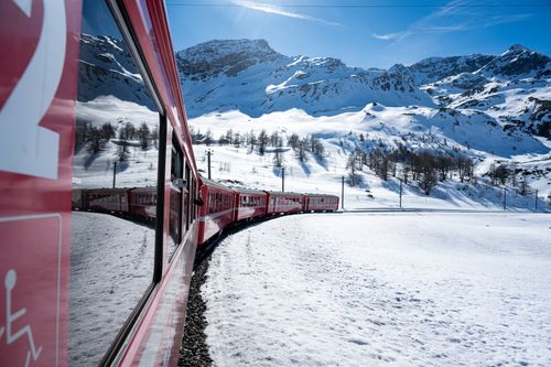 Free A picturesque red train curves through snowy alpine terrain under a clear blue sky. Stock Photo
