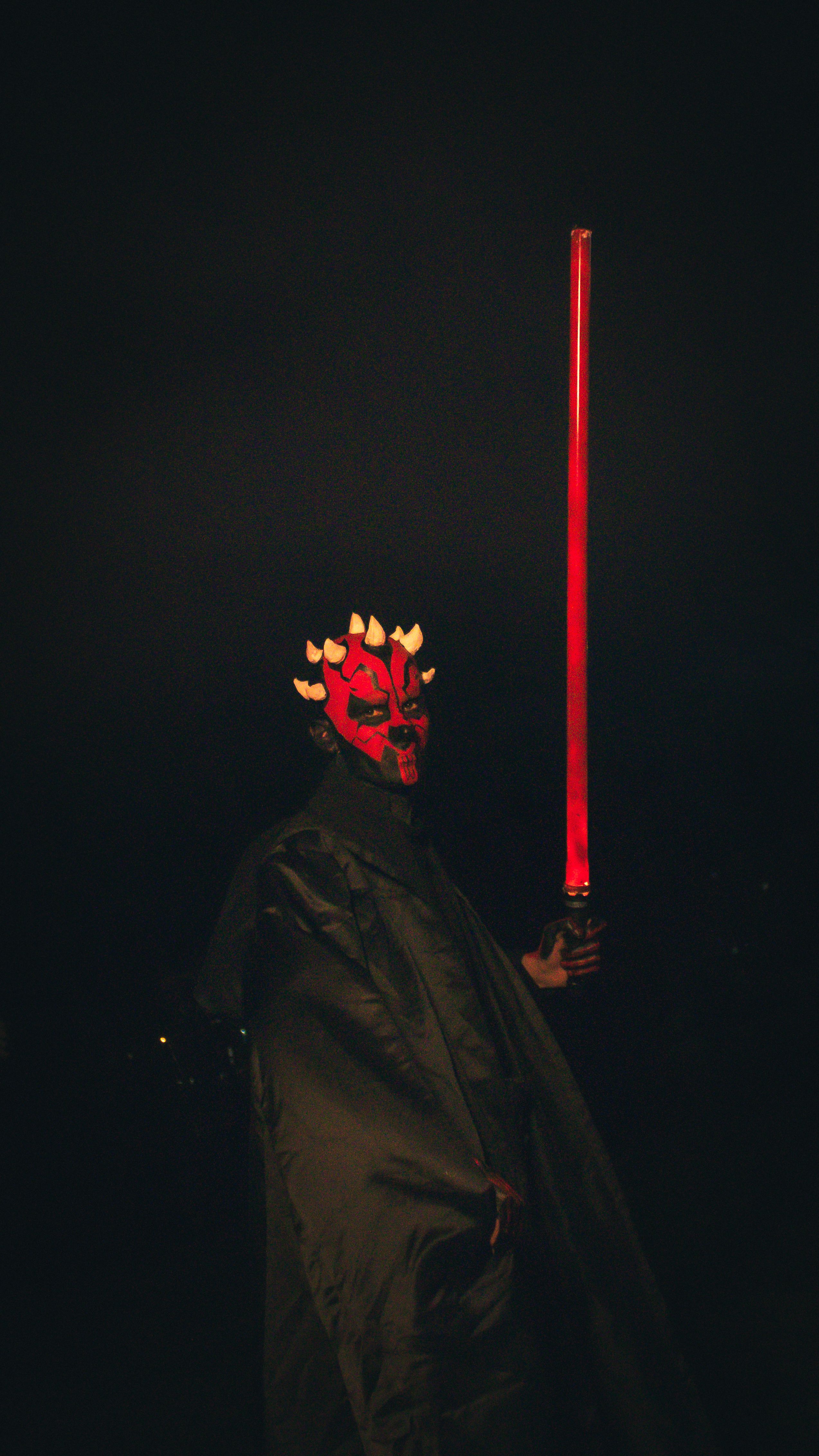 A person dressed as a dark fantasy character holding a glowing red lightsaber, captured at night.