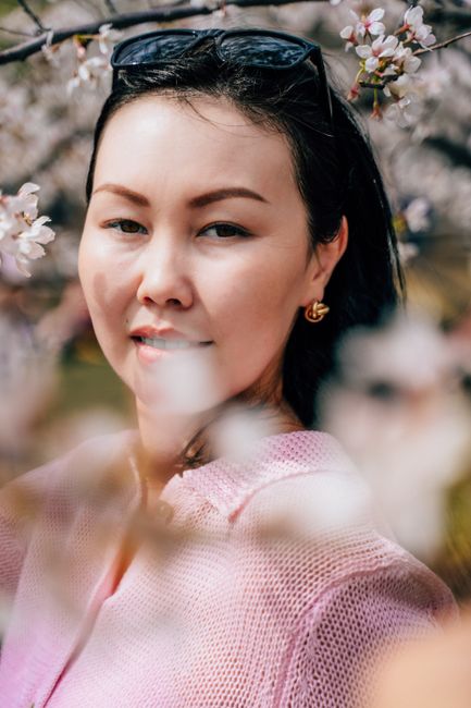 Portrait of an Asian woman in a pink sweater with cherry blossoms in spring. Soft lighting and pastel colors create a serene mood.