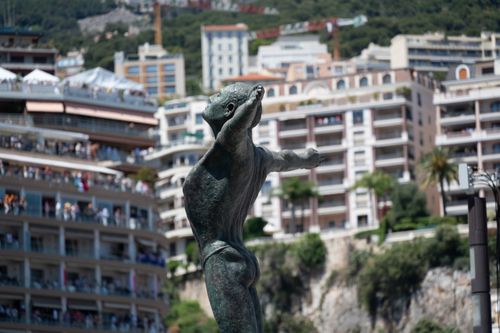 Free A statue amid Monaco's urban landscape with a distant crowd and lush greenery. Stock Photo