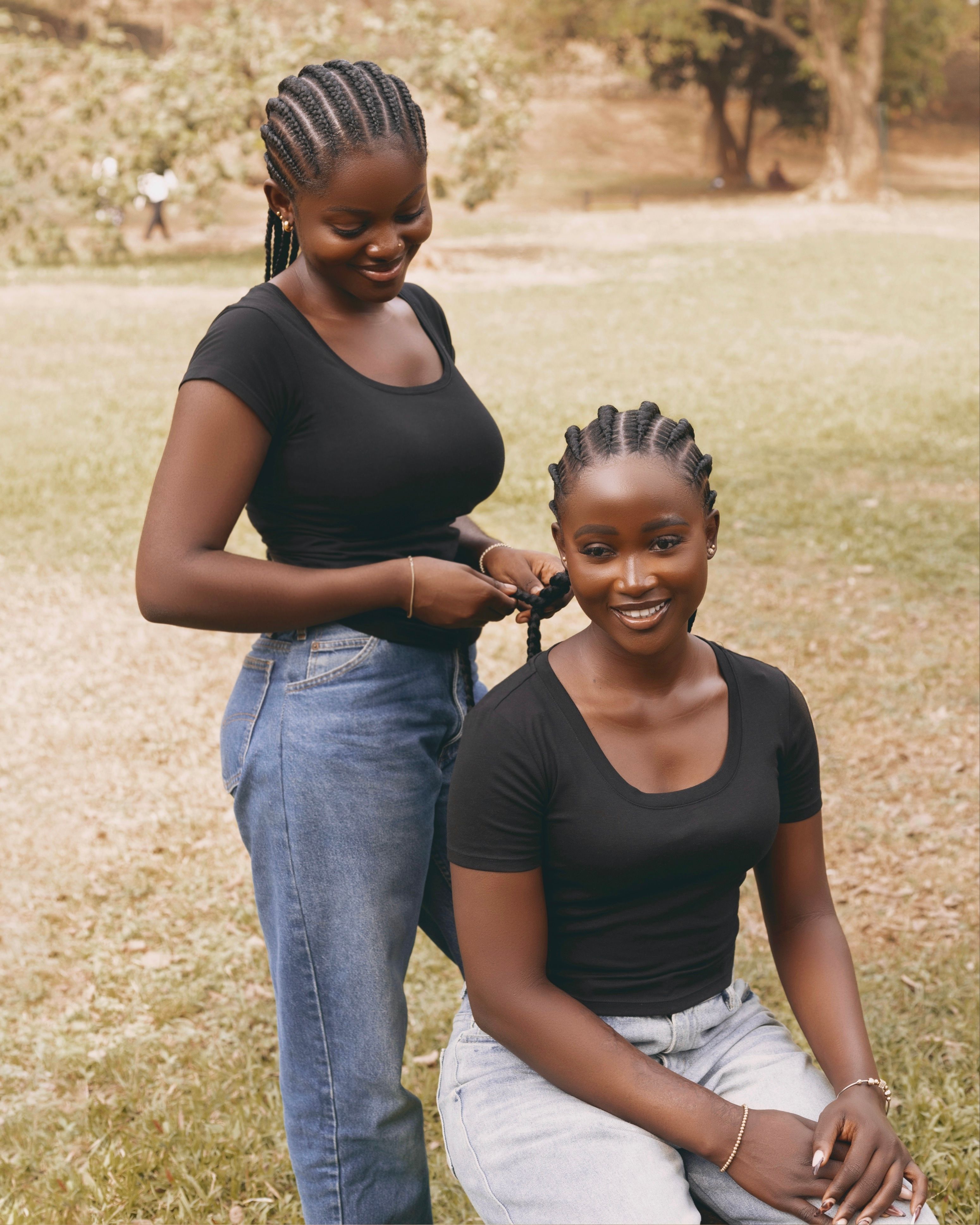 Two young women braiding hair outdoors in Abuja, showcasing friendship and style.