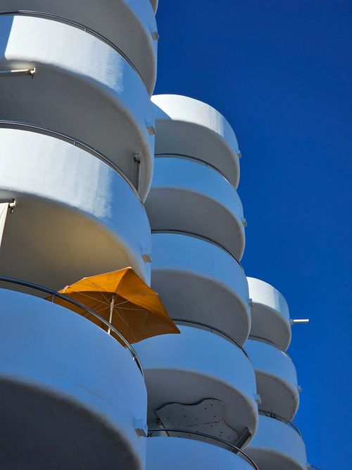 Free Artistic view of modern circular balconies against a deep blue sky with an orange umbrella. Stock Photo