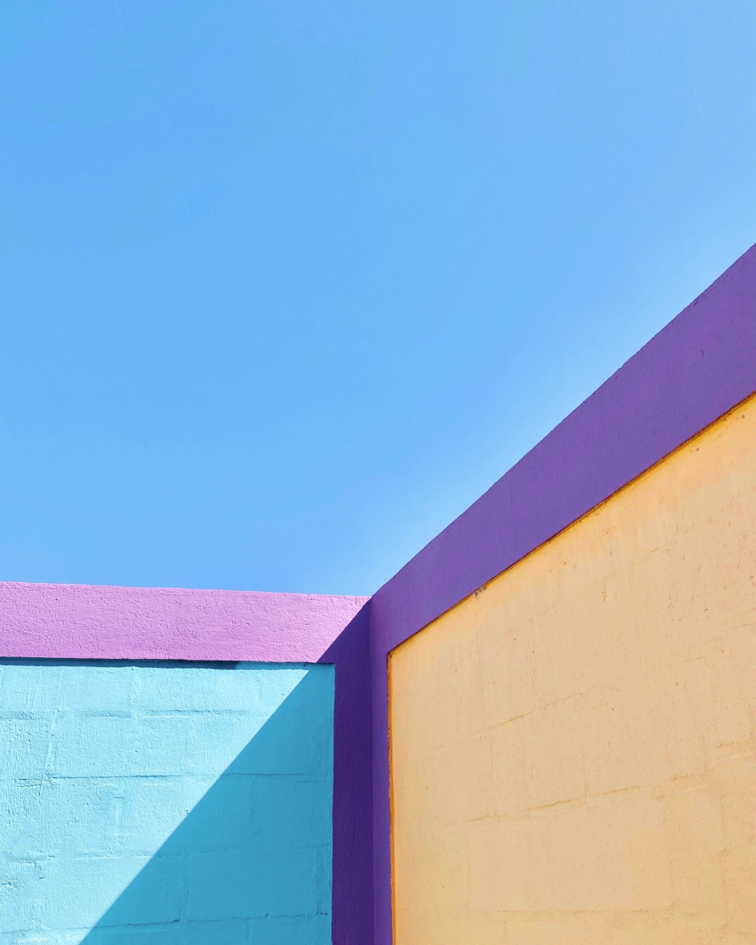 Colorful pastel walls forming a geometric composition under a clear blue sky, highlighting vibrant modern architecture.