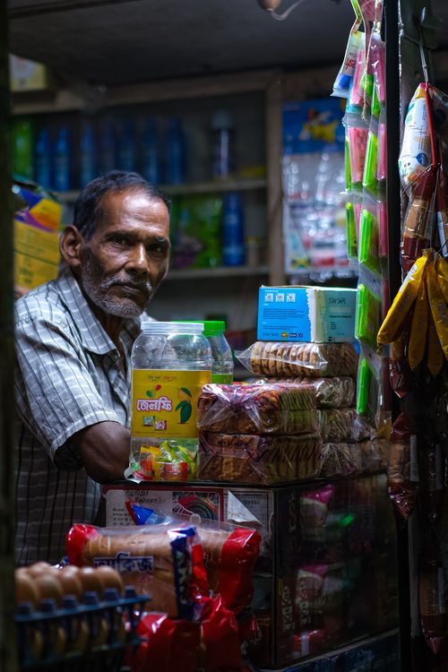 Free Portrait of a shopkeeper surrounded by goods in a bustling marketplace, showcasing local commerce. Stock Photo