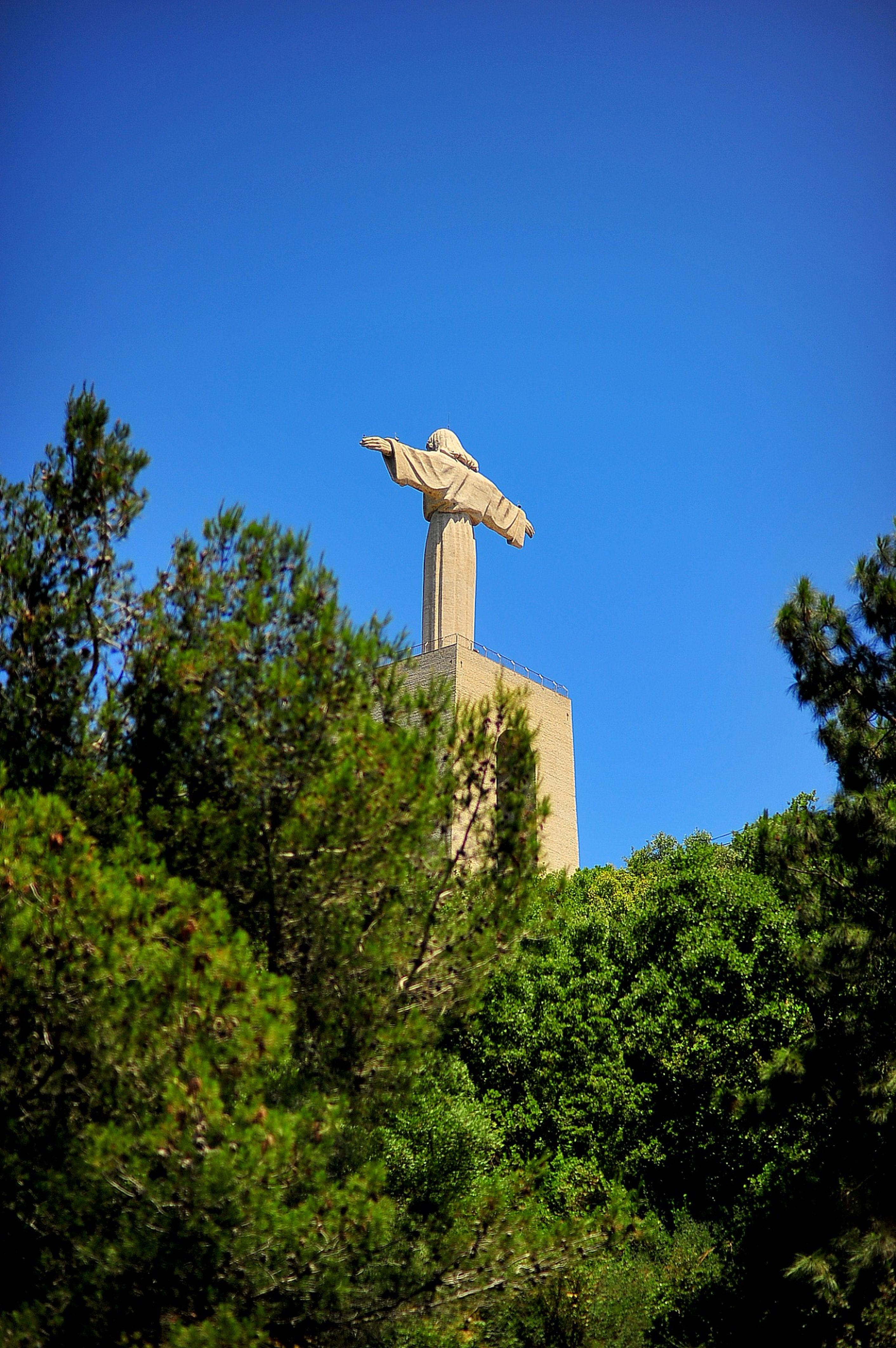 Stunning view of the Cristo Rei statue in Almada, framed by lush greenery against a clear blue sky.
