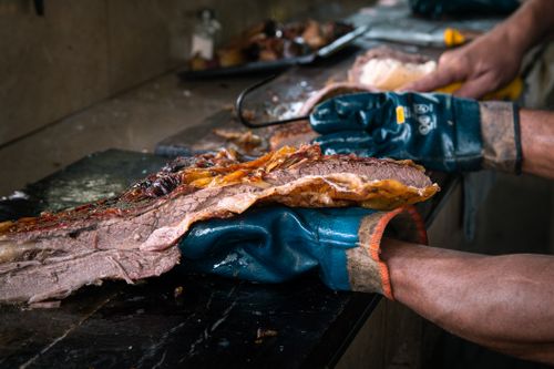 Free Close-up of a gloved chef slicing a succulent, grilled beef brisket in a kitchen setting. Stock Photo