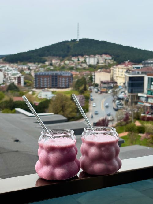 Free Two pink smoothies in unique glasses with a scenic city view in the background. Stock Photo