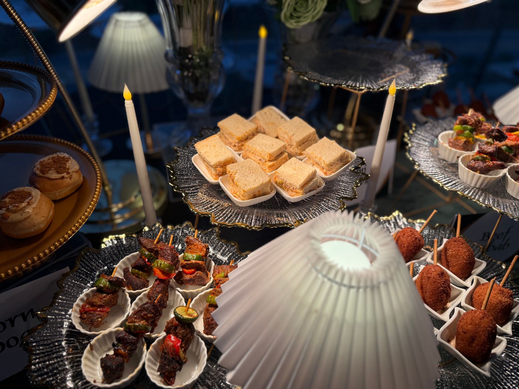 A luxurious spread of assorted appetizers on ornate platters, illuminated by candlelight.
