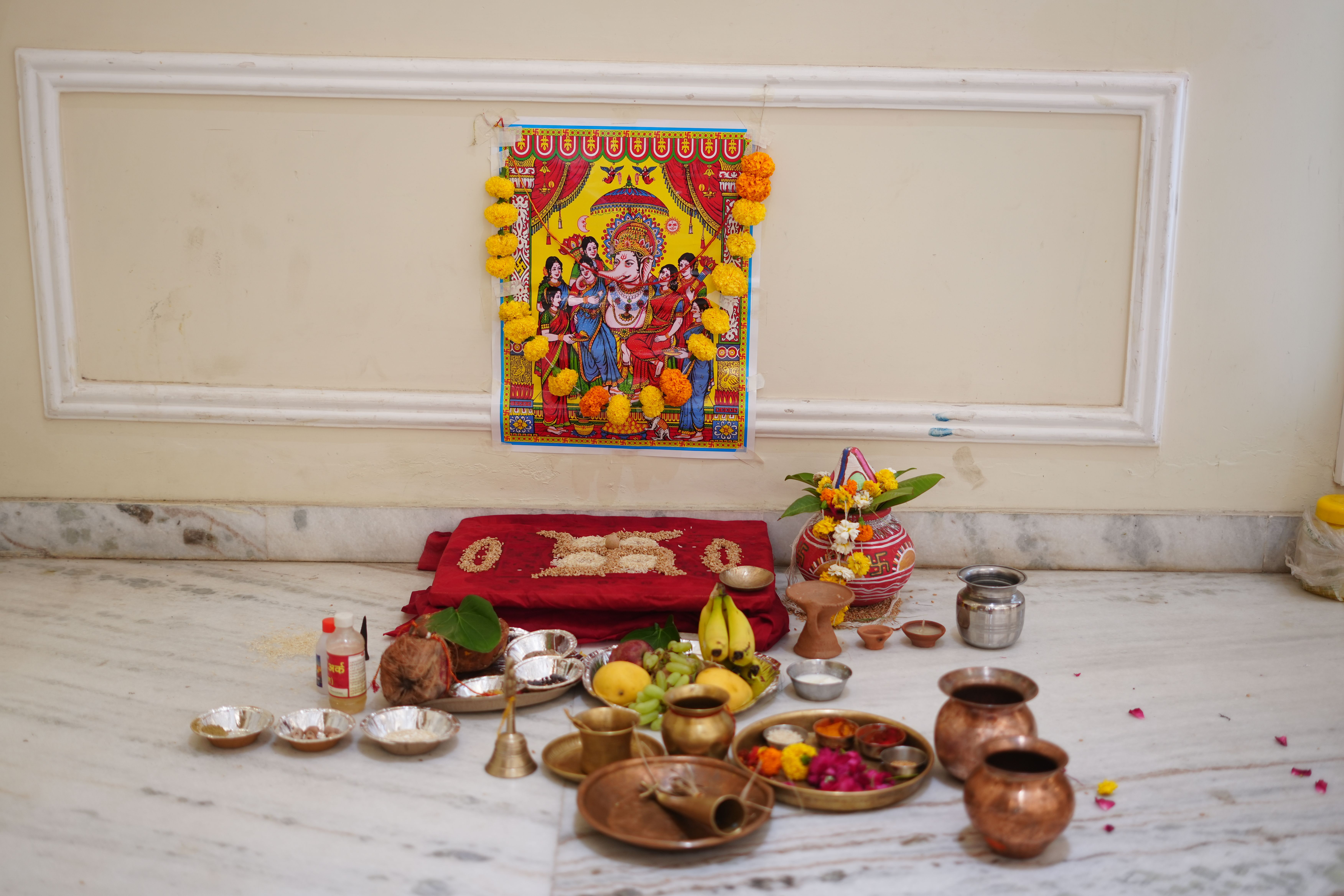 A detailed setup for a traditional Ganesh puja featuring marigold garlands, fruits, and copper utensils.
