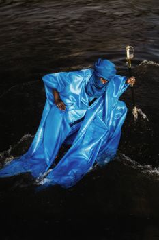 A man dressed in a vibrant blue robe sits by the water, showcasing vibrant Nigerian culture.