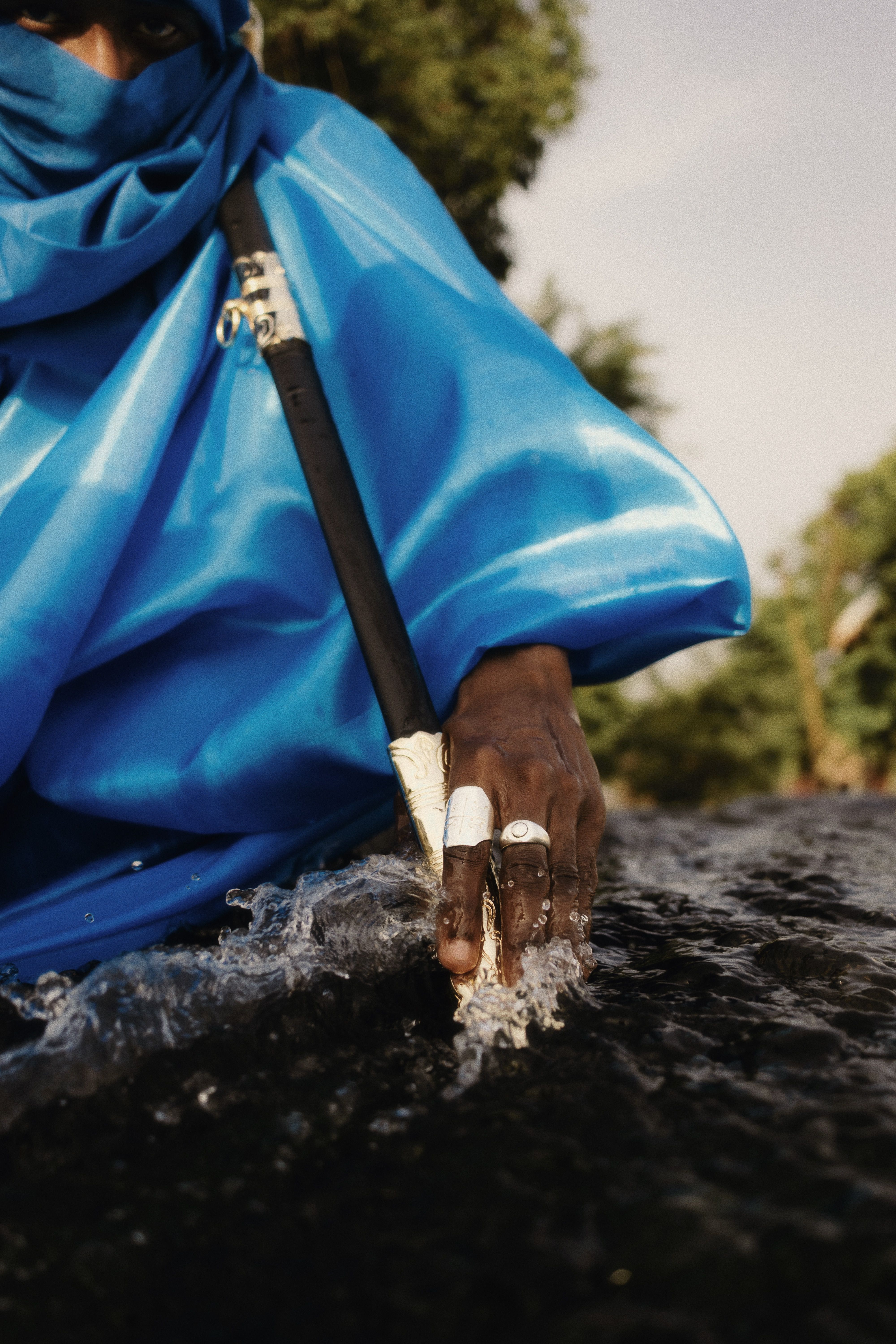 A man in a blue robe touching water, showcasing cultural attire in Nigeria.