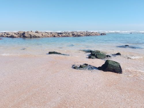 Free Tranquil beach scene featuring a rocky shoreline with gentle waves under a clear blue sky. Stock Photo