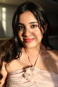 A close-up portrait of a young woman with a gentle smile, captured in warm natural light indoors.