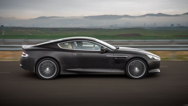 A sleek black car speeds down a highway with scenic views in Kurdistan, Iraq.
