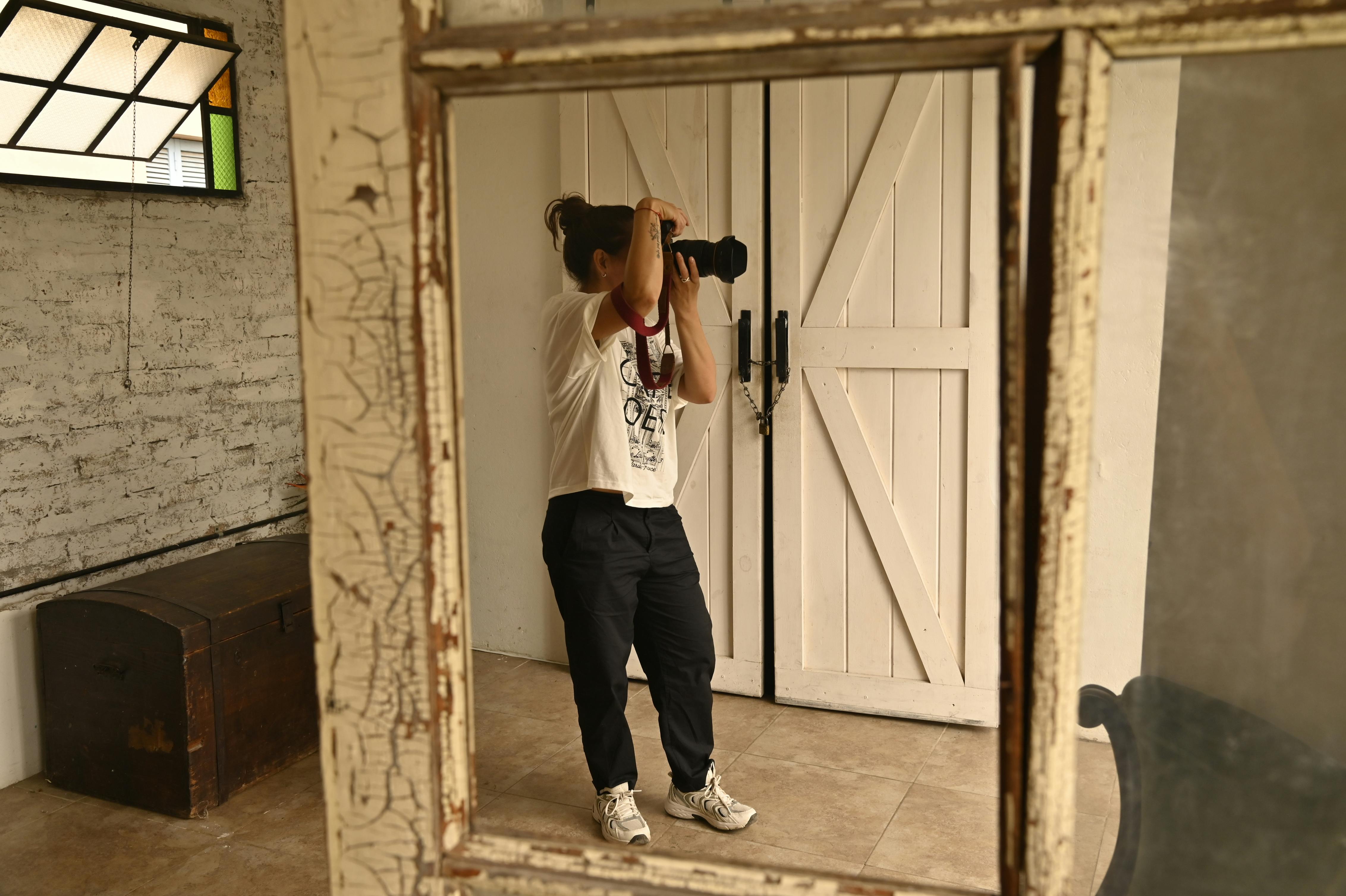A photographer taking a picture indoors, reflected in a mirror with rustic decor.