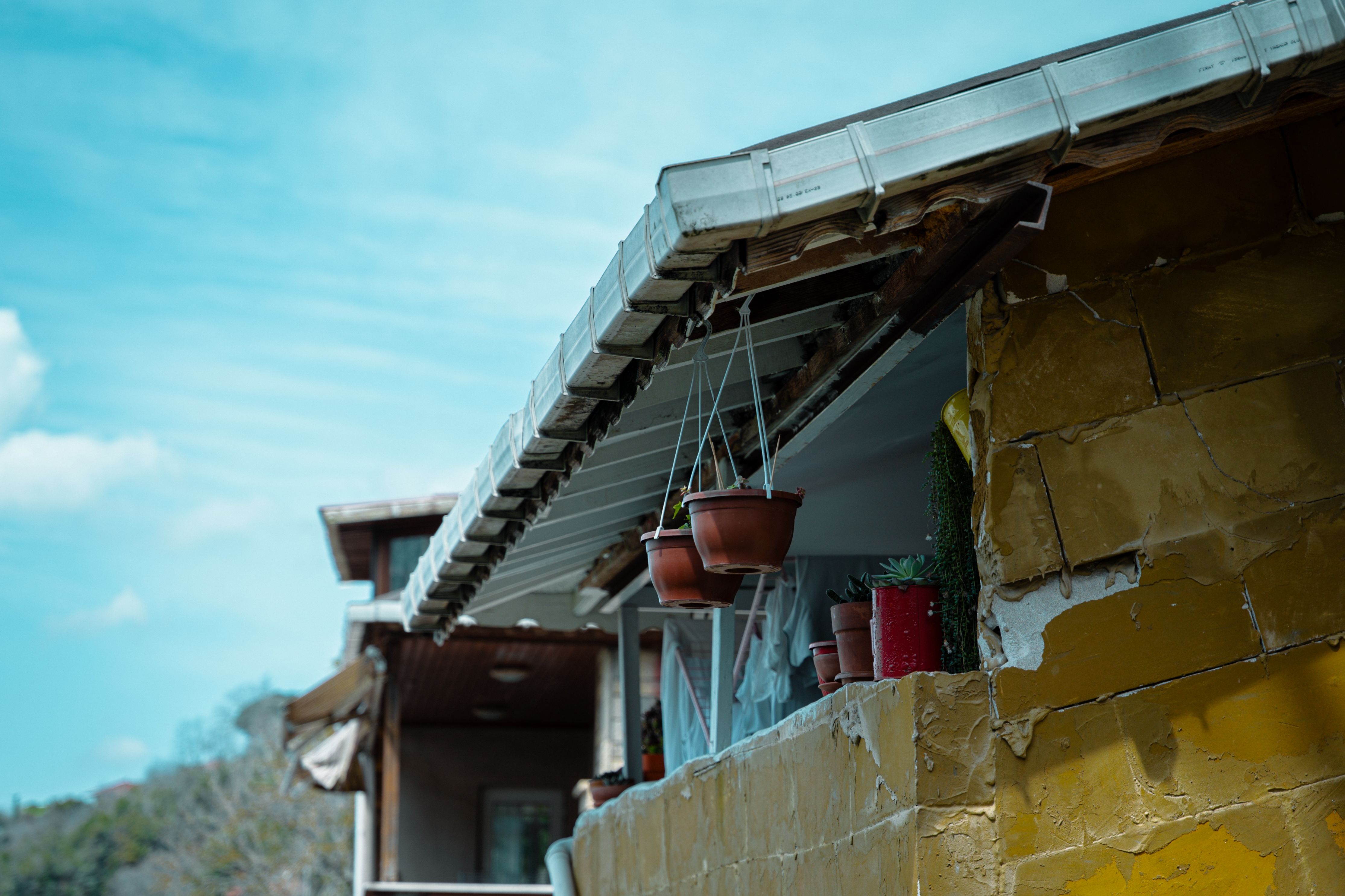 Rustic yellow house exterior with hanging plants under a bright blue sky.