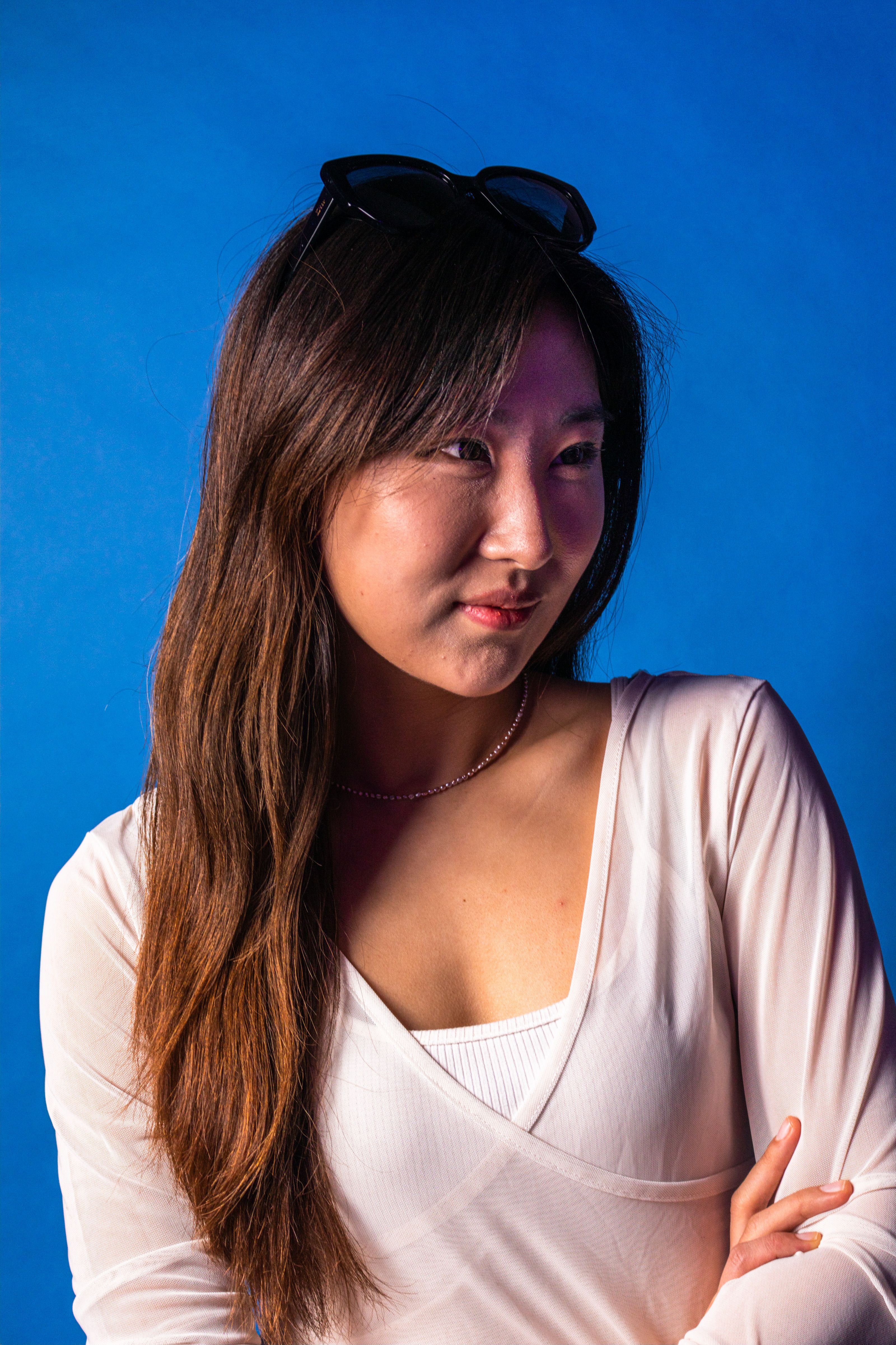 Portrait of a smiling woman in a white top with sunglasses on her head against a vibrant blue backdrop.