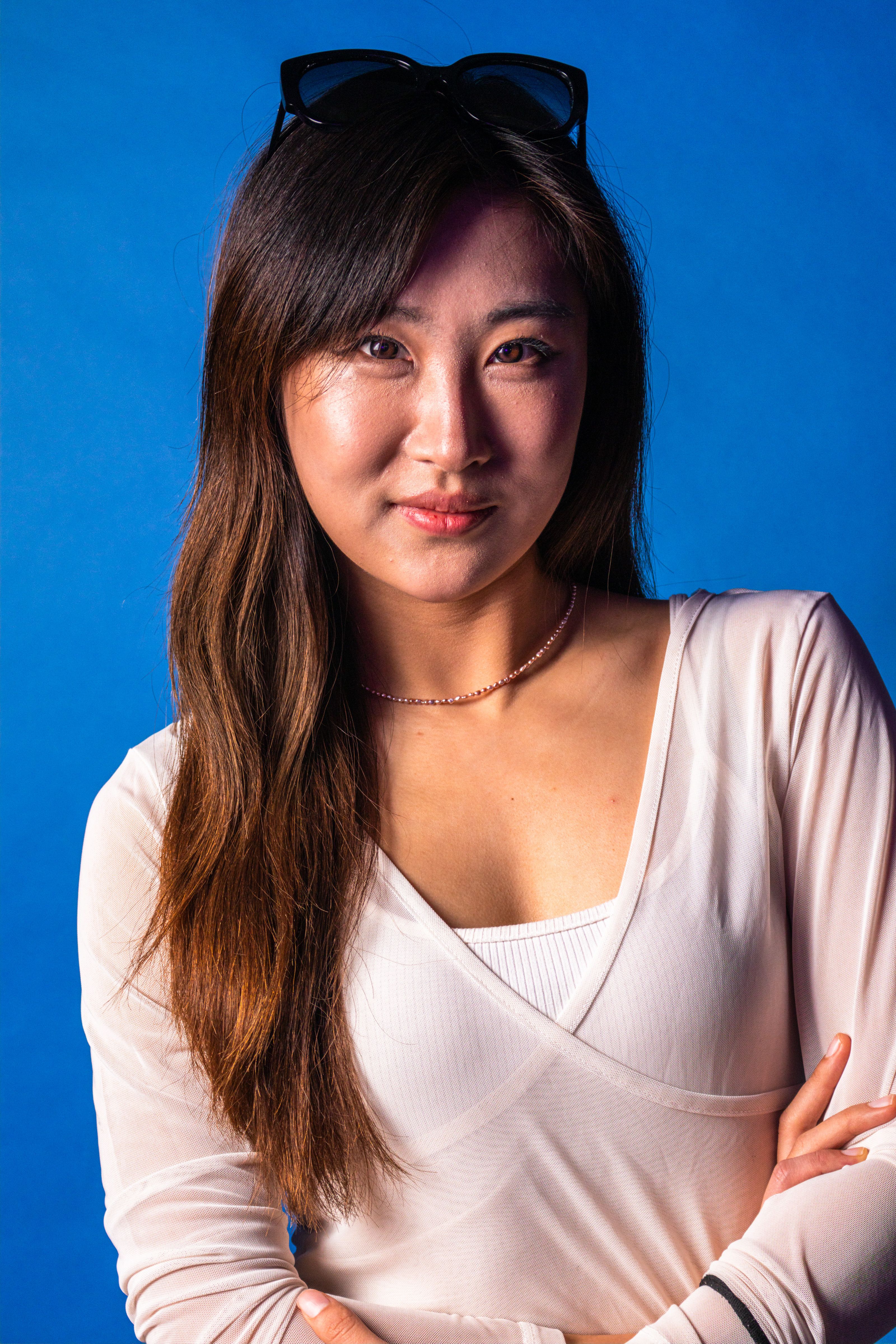 Confident woman in a white top stands against a vivid blue background, smiling softly.