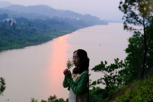 A serene portrait of a young woman by the Huong River in Huế, Vietnam, at sunset, evoking tranquility and cultural beauty.