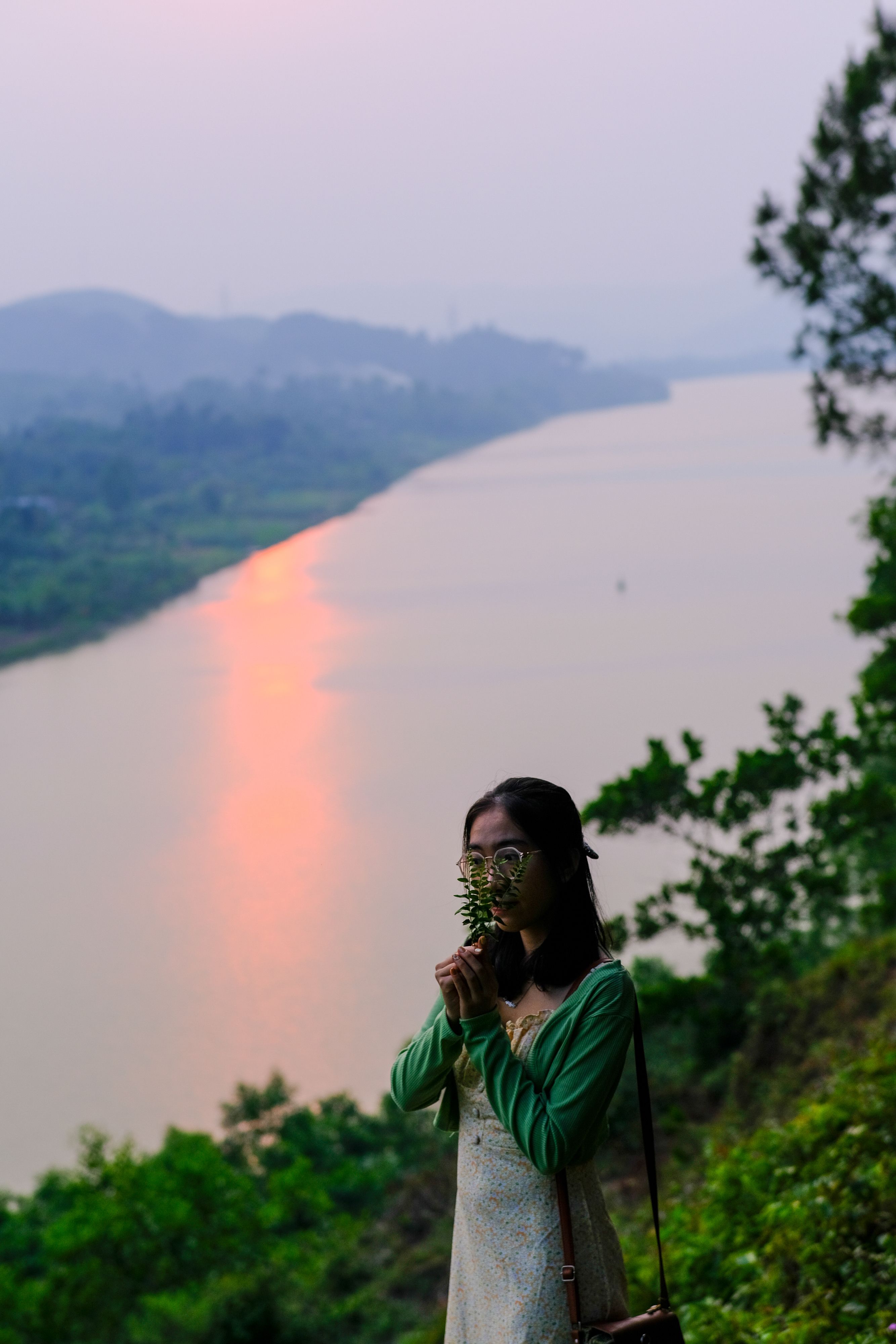 A woman enjoys a peaceful moment by the Perfume River in Huế, Vietnam during sunset.