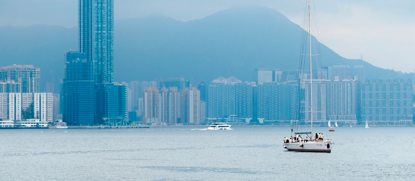 Peaceful sailboat cruising on Hong Kong Island's waterfront with city skyline backdrop.