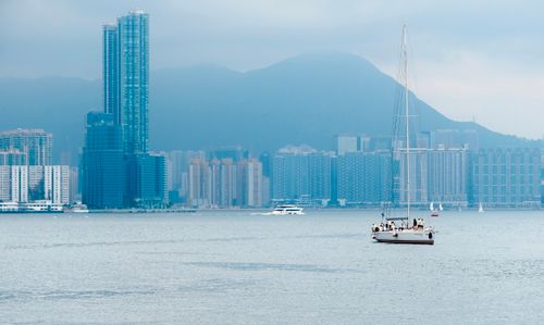 Free Peaceful sailboat cruising on Hong Kong Island's waterfront with city skyline backdrop. Stock Photo