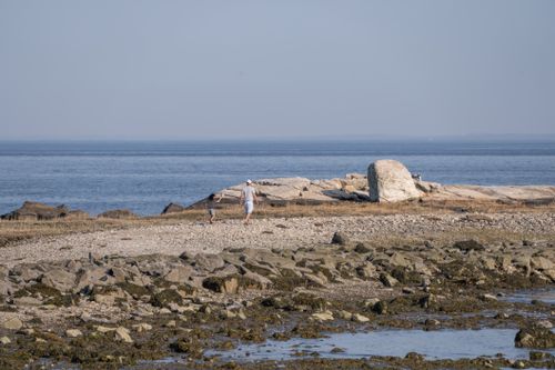 Free Two people enjoy a walk on a rocky beach with distant ocean view, clear sky, and serene atmosphere. Stock Photo