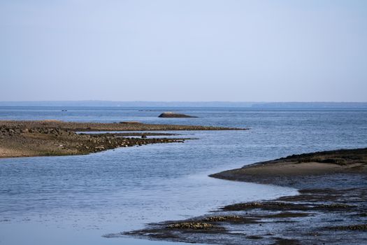 Tranquil coastal shoreline at low tide with calm blue ocean and distant horizon.