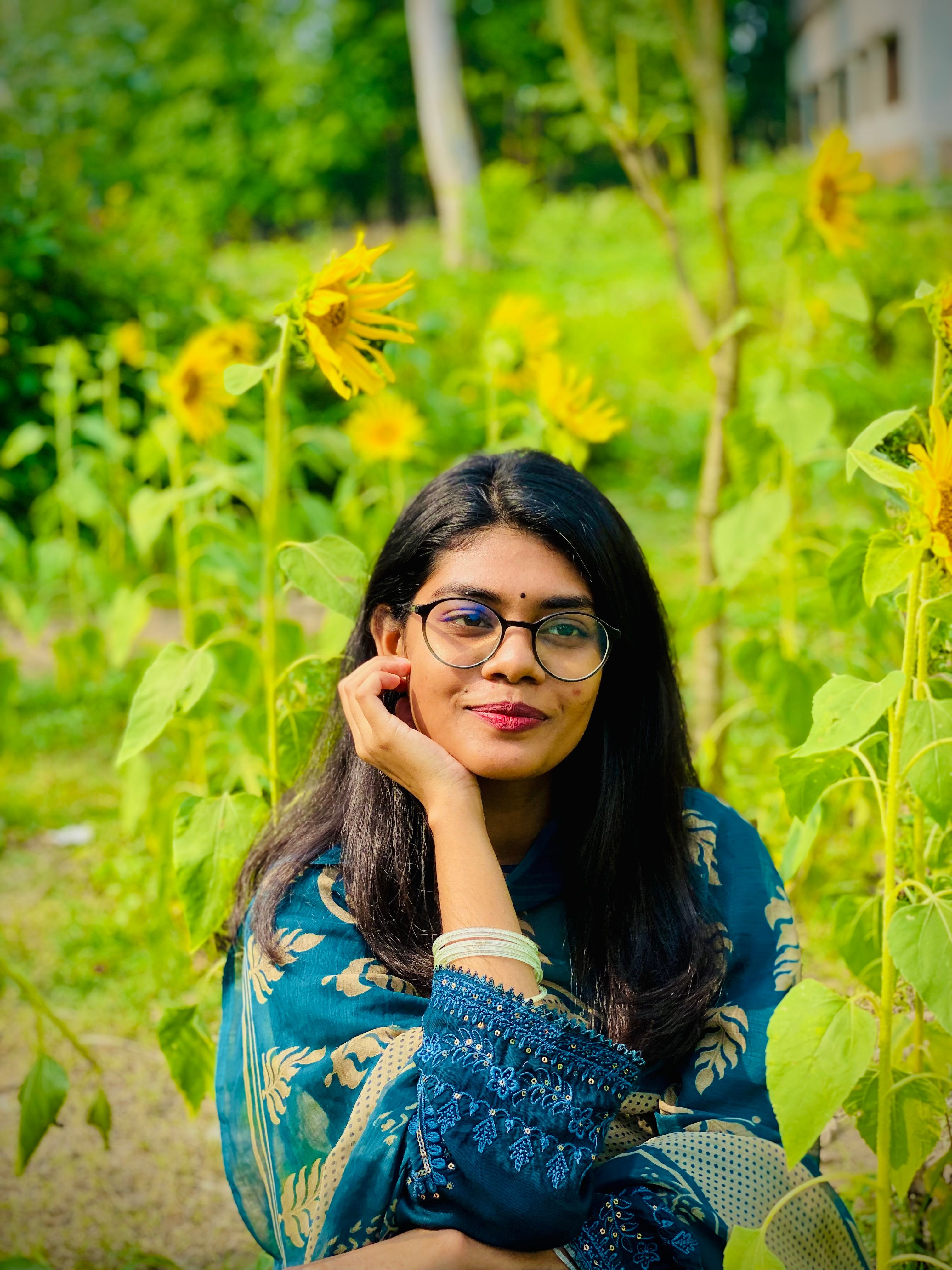 Smiling woman in traditional attire surrounded by vibrant sunflowers.