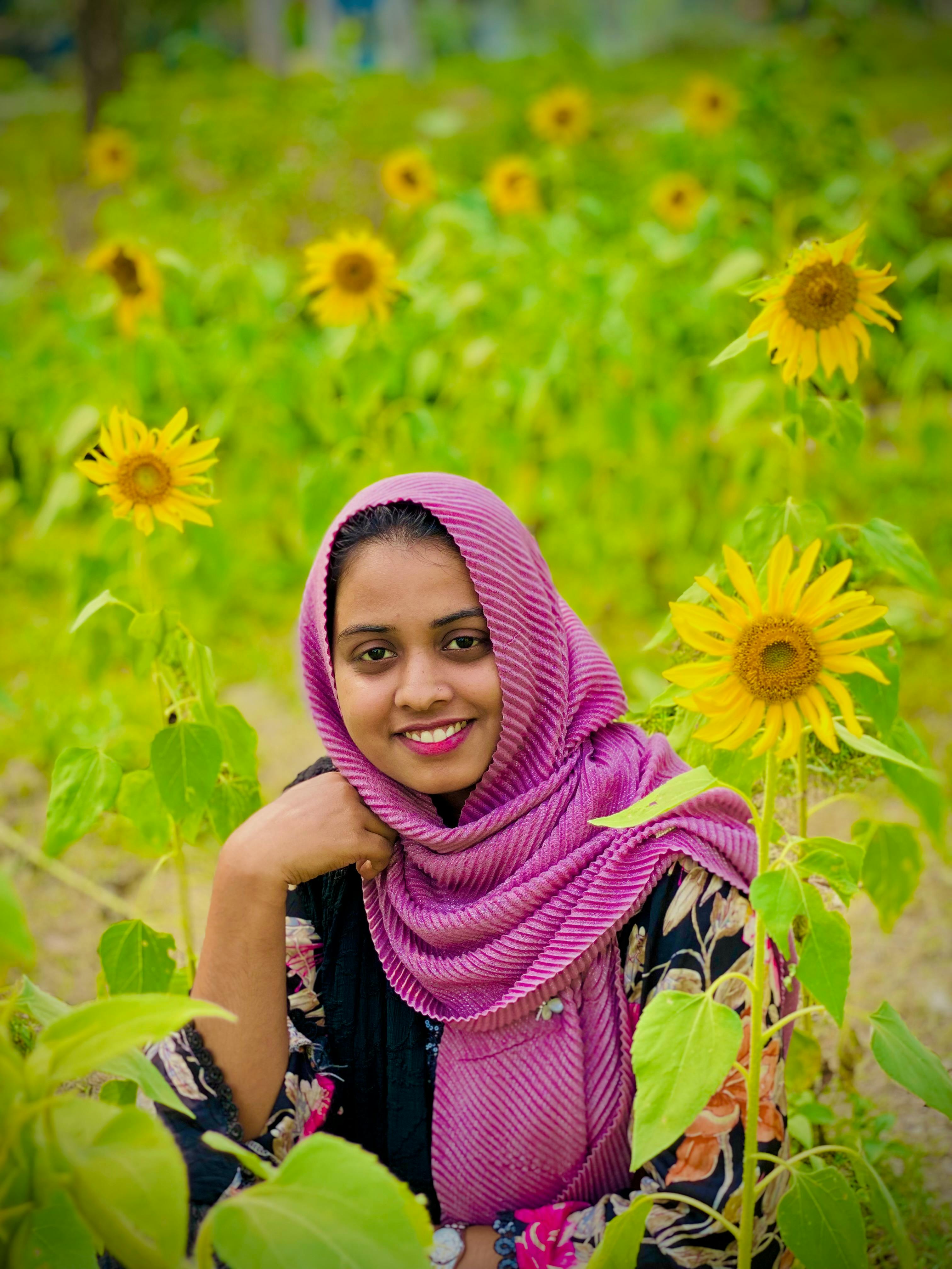 Smiling woman in a colorful scarf enjoys the blooming sunflower field