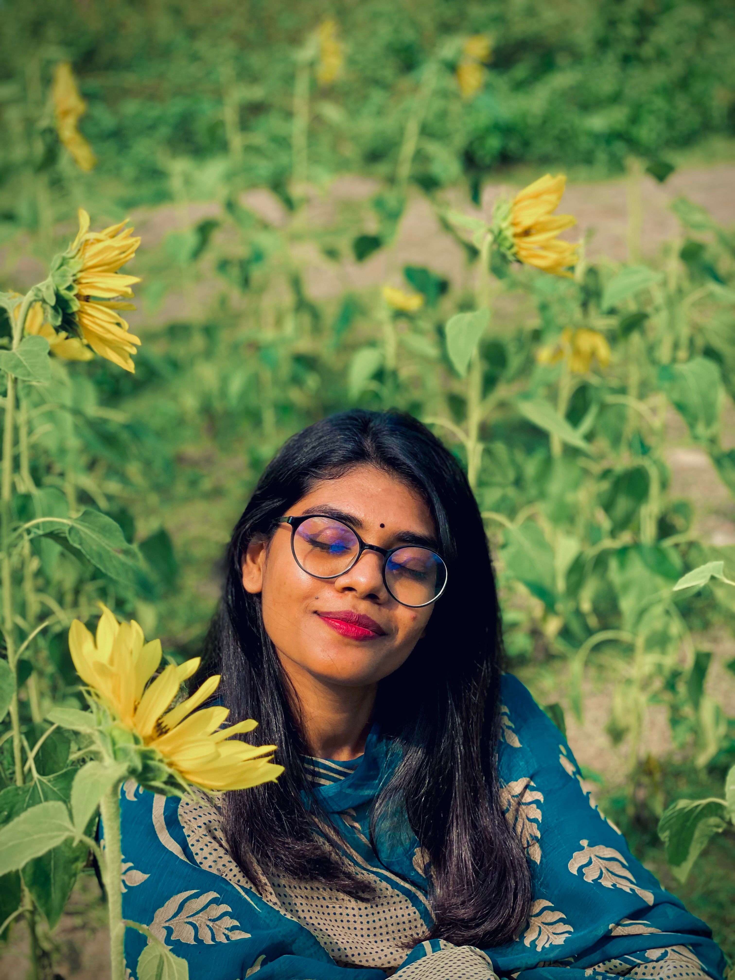 Serene young woman with glasses poses peacefully in a sunflower field, embracing nature.