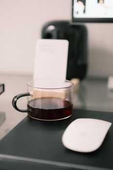 A clean, minimalist workspace featuring a glass cup of coffee and a computer mouse on a mousepad.
