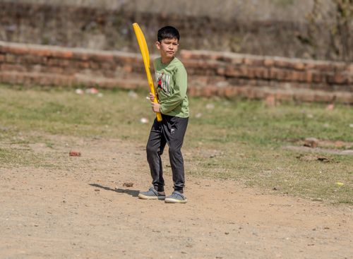 Free A young boy stands ready with a yellow bat, playing cricket outside on a sunny day. Stock Photo