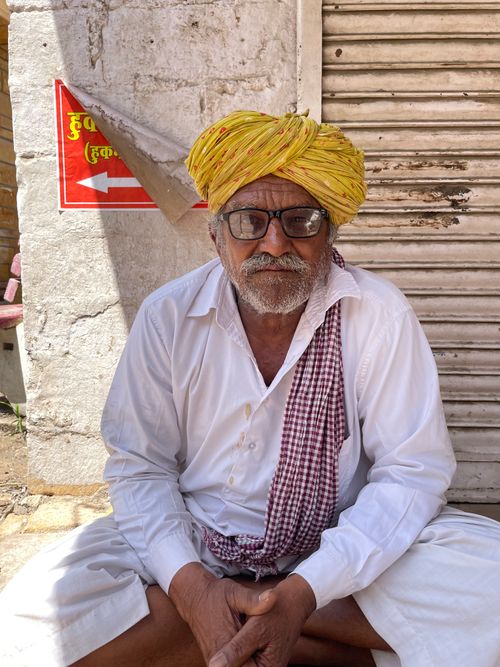 Free An elderly man sits outdoors in Jaisalmer, wearing a traditional yellow turban and spectacles. Stock Photo