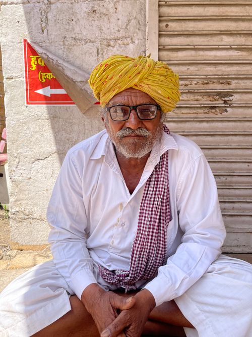 Free Elderly Indian man wearing a yellow turban, seated against a wall in Jaisalmer. Stock Photo