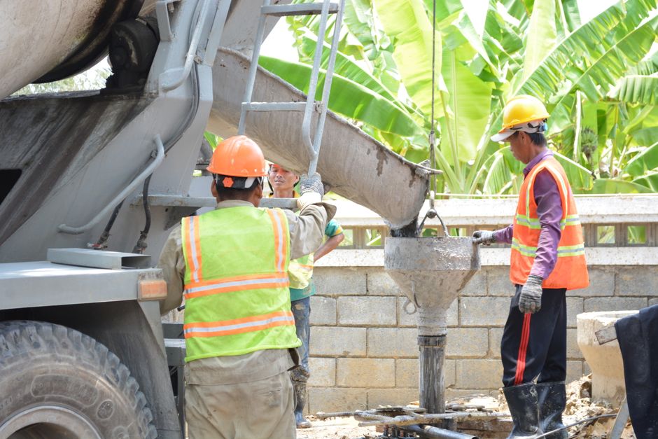 Construction workers managing cement pour from a mixer on site, wearing safety gear outdoors.