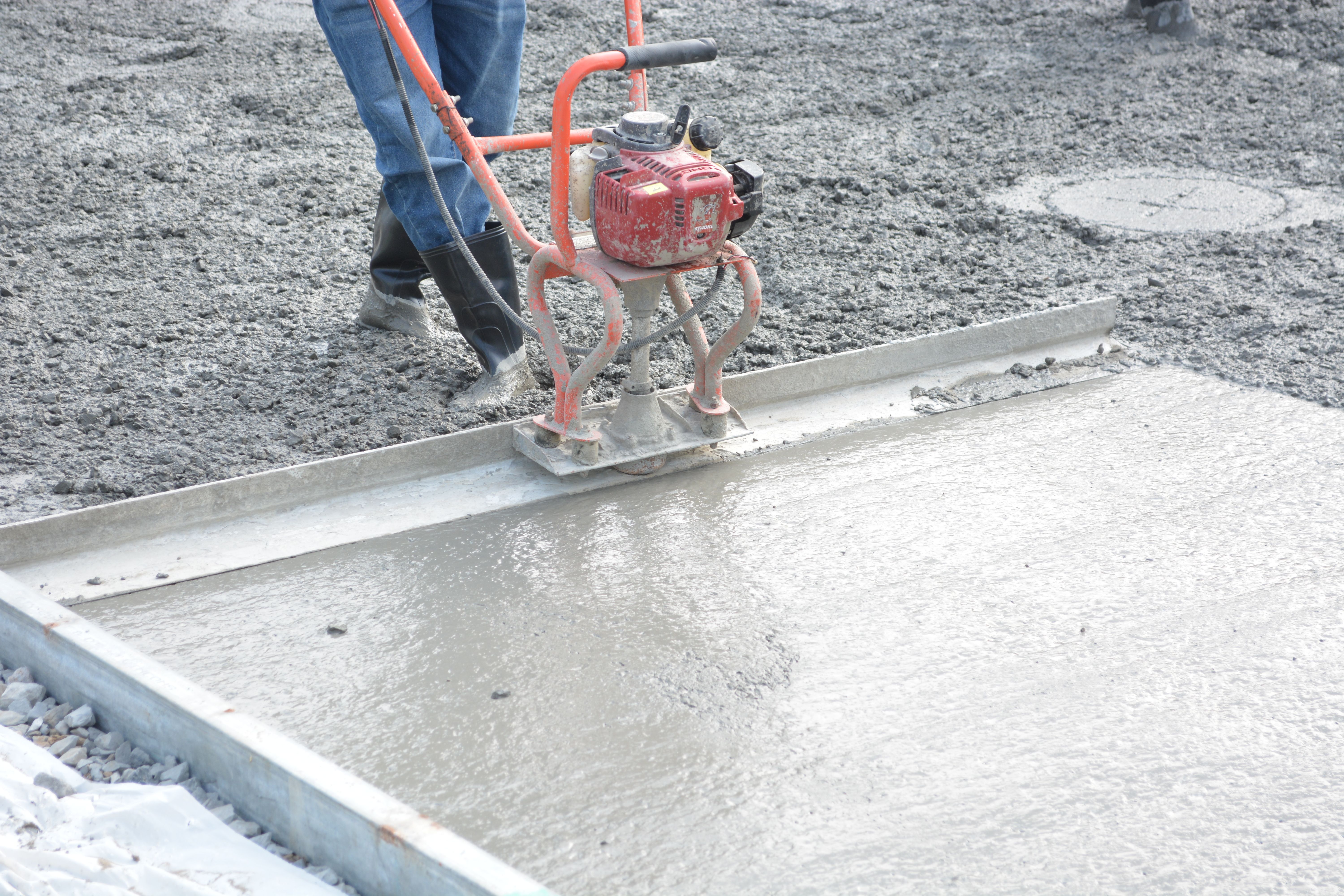 A construction worker opera tes a power trowel to smooth freshly poured concrete on a construction site
