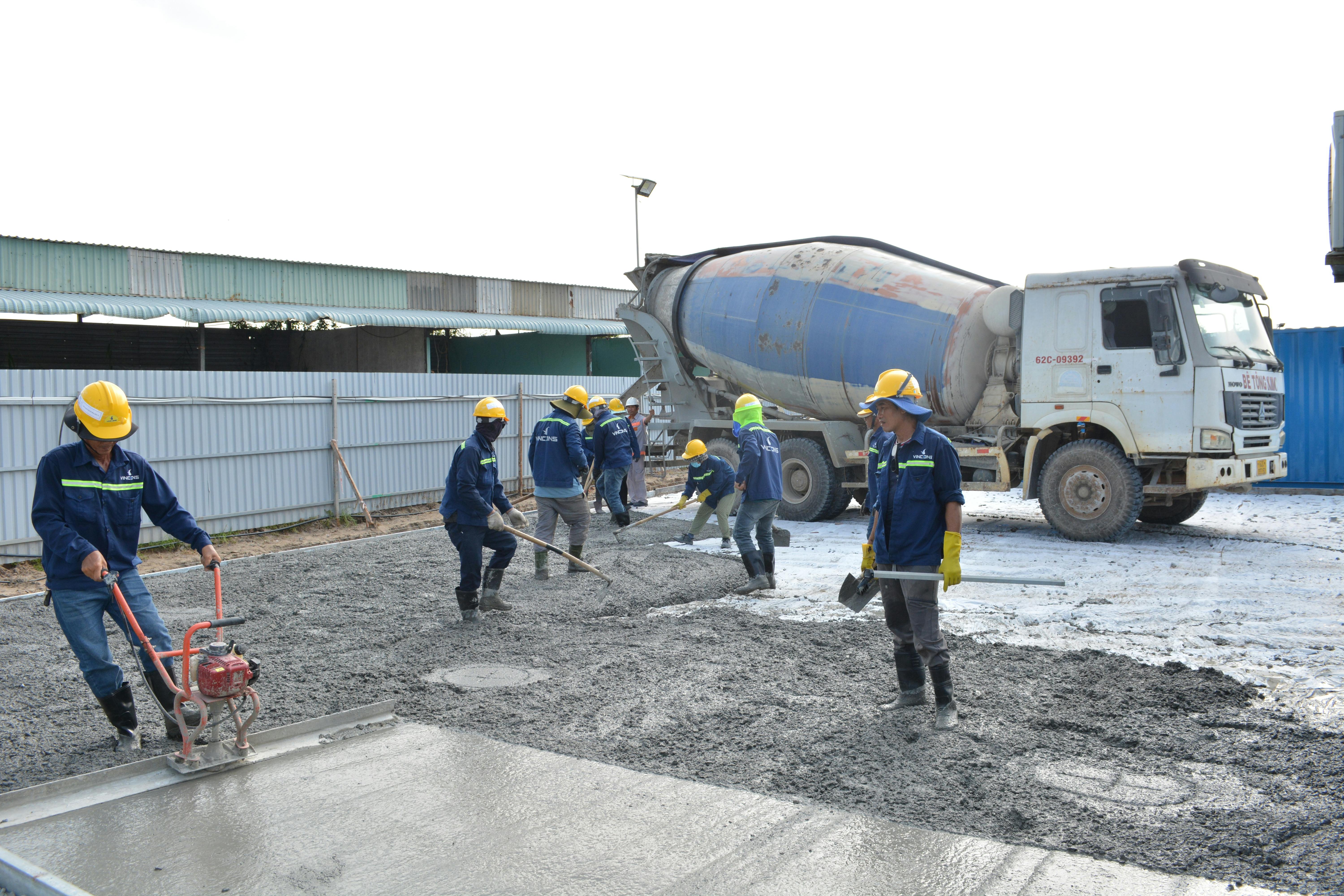 Workers in safety gear at a concrete pour, rig staged on outdoor site.