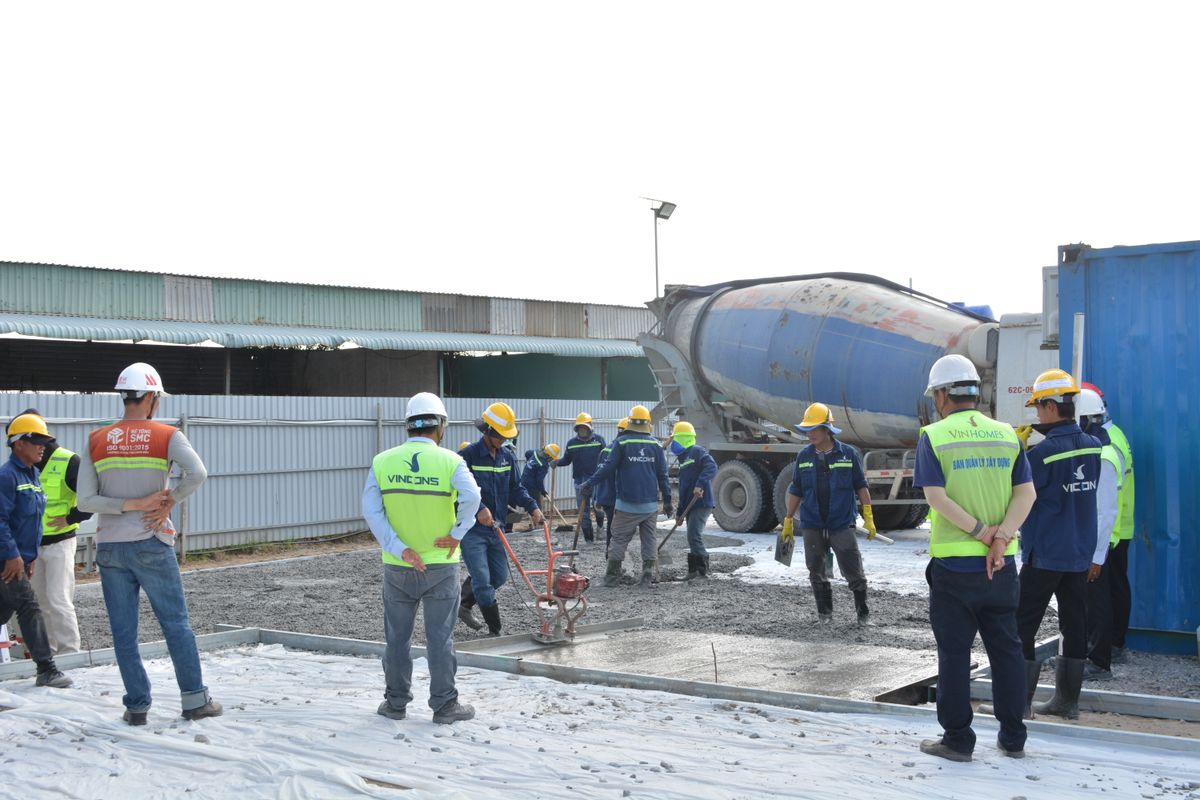 Team of workers in helmets and safety vests working together on a construction site with a cement mixer truck