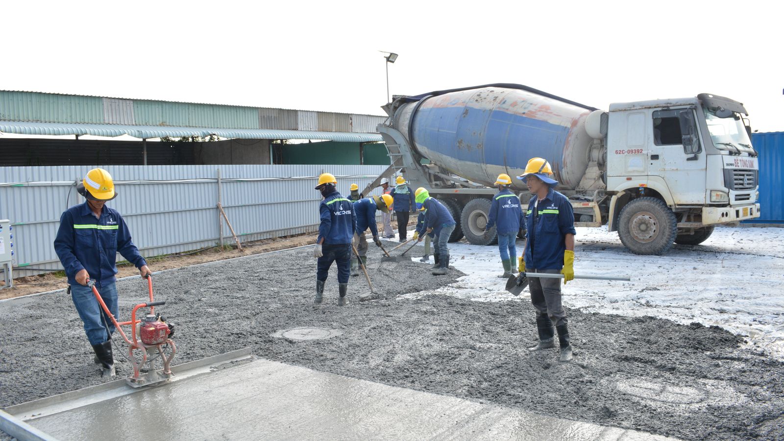Concrete agitator truck on site while a crew spreads and levels a fresh slab pour
