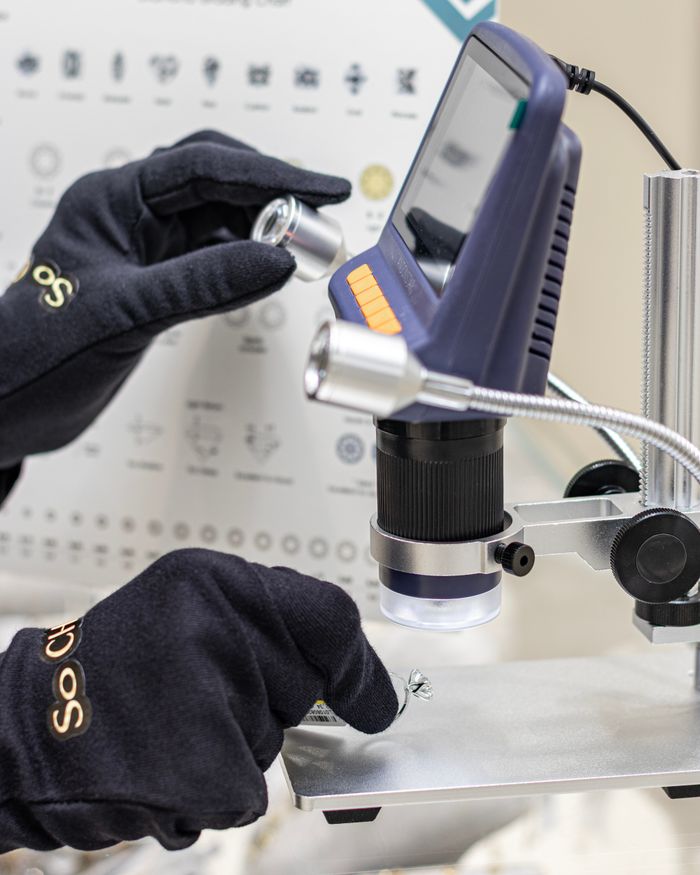 Gloved hands inspecting a part under a digital microscope