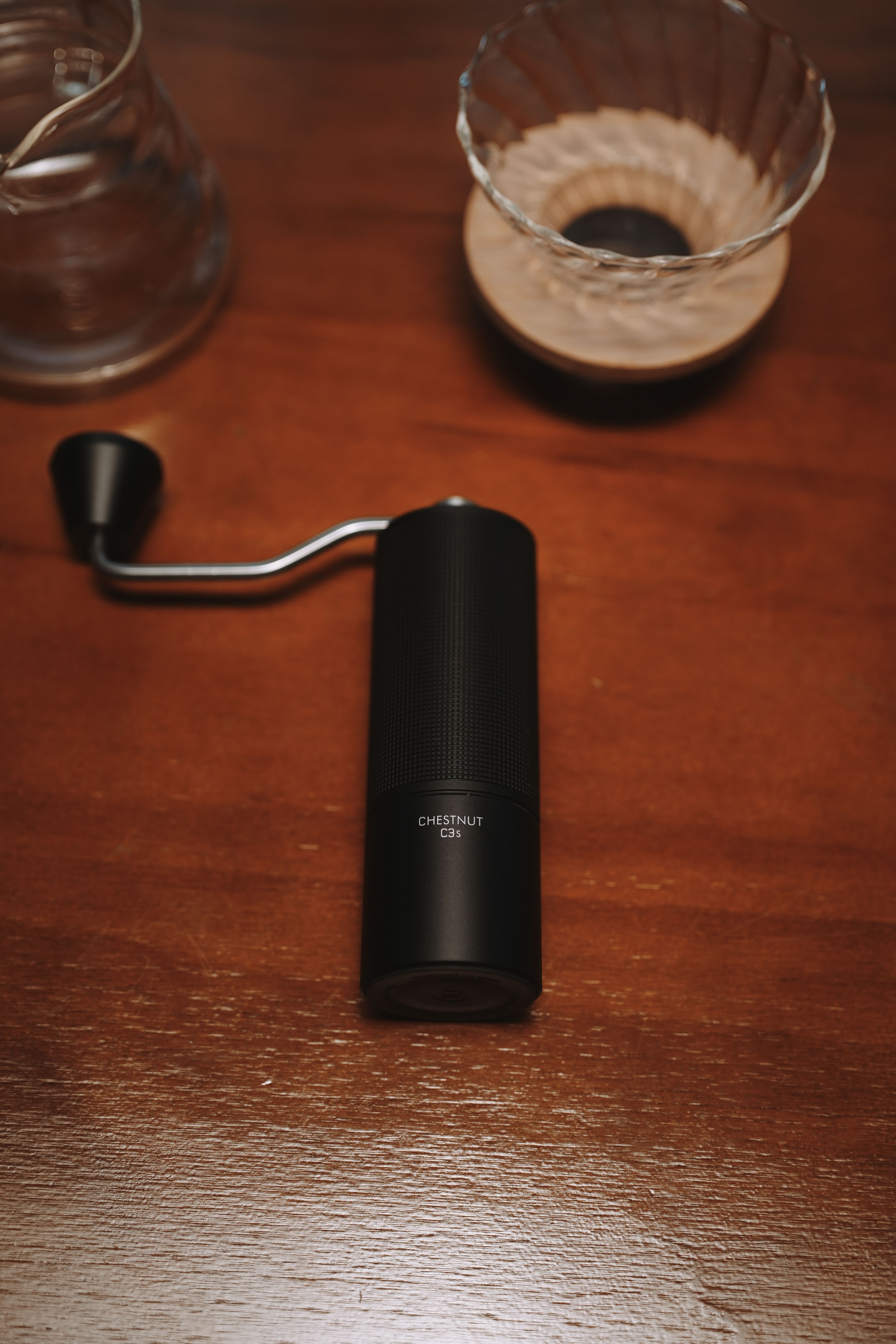 Stylish manual coffee grinder on a wooden table with coffee brewing accessories.