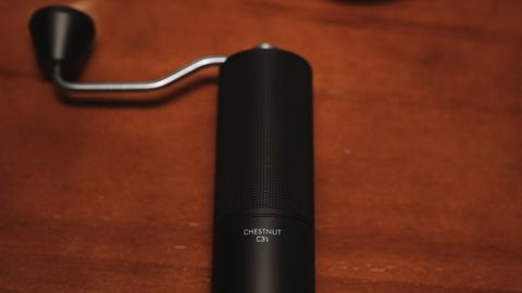 Stylish manual coffee grinder on a wooden table with coffee brewing accessories.