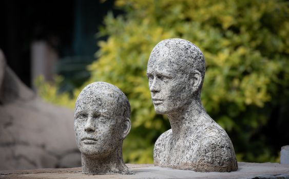 Two lifelike stone sculptures of faces against a leafy backdrop, showcasing artistic craftsmanship.