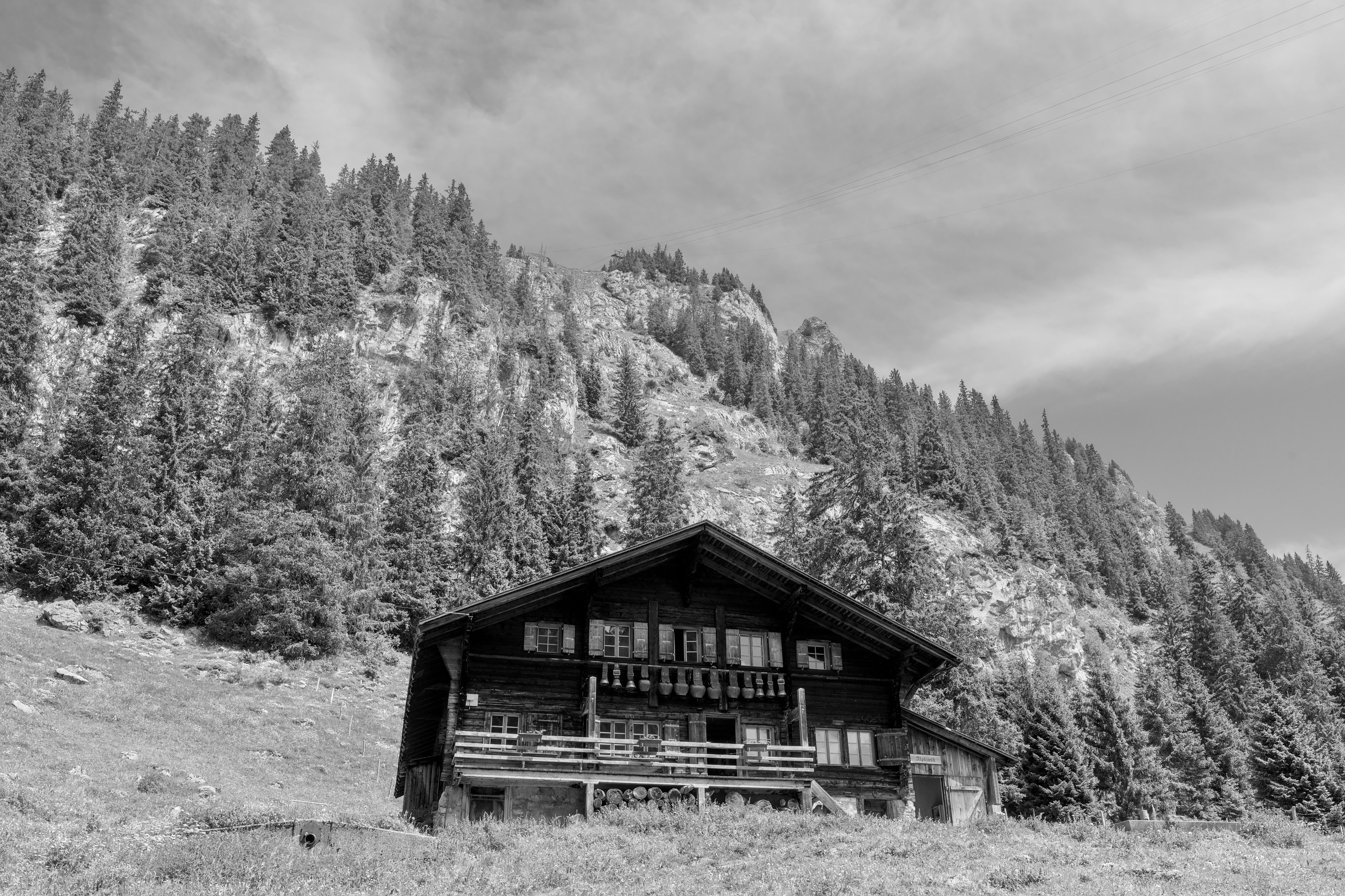 Photo en noir et blanc d'un chalet suisse traditionnel niché dans les montagnes alpines.