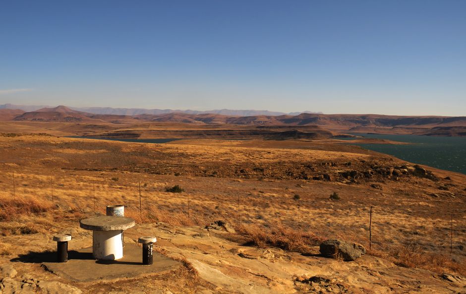 Panoramic view of a vast, arid landscape with a dam and a distant mountain range under a clear sky.
