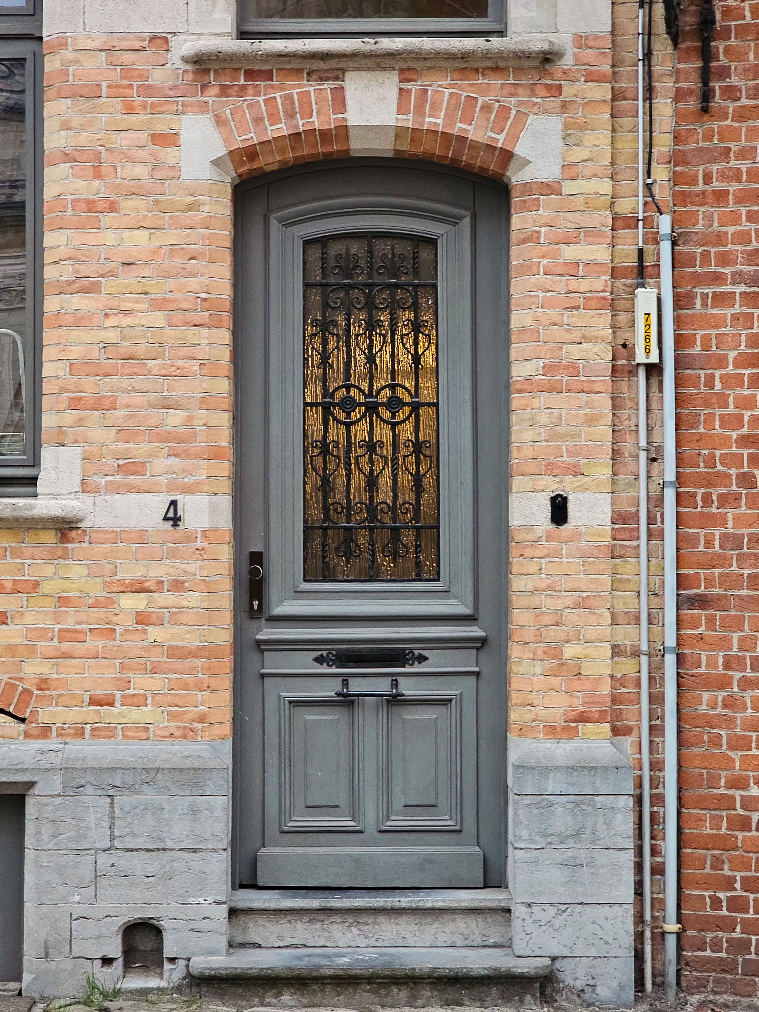 Grey wooden door with ornate ironwork set in a brick building façade.