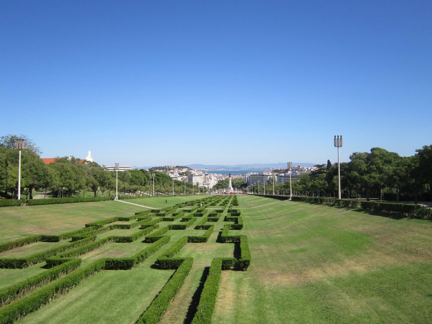 A beautiful view of Lisbon's Edward VII Park, showcasing manicured hedges and cityscape under a clear blue sky.